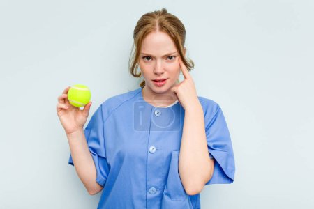 Photo for Young caucasian physiotherapist holding a tennis ball isolated on blue background showing a disappointment gesture with forefinger. - Royalty Free Image