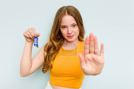 Foto de Young caucasian woman holding home keys isolated on blue background standing with outstretched hand showing stop sign, preventing you. - Imagen libre de derechos
