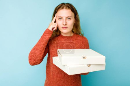 Photo for Young caucasian woman holding pizzas boxes isolated on blue background pointing temple with finger, thinking, focused on a task. - Royalty Free Image