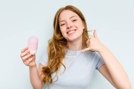 Téléchargez les photos : Jeune femme caucasienne tenant déodorant isolé sur fond bleu montrant un geste d'appel téléphonique mobile avec les doigts. - en image libre de droit