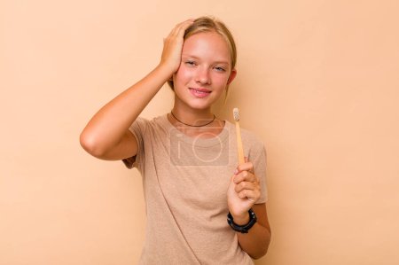 Foto de Caucásico adolescente chica cepillarse los dientes aislado en beige fondo siendo impactado, ella ha recordado importante reunión. - Imagen libre de derechos