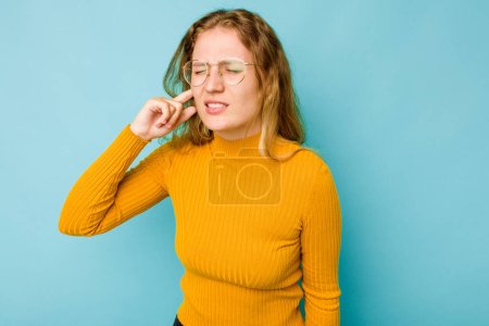 Photo for Young caucasian woman isolated on blue background covering ears with fingers, stressed and desperate by a loudly ambient. - Royalty Free Image