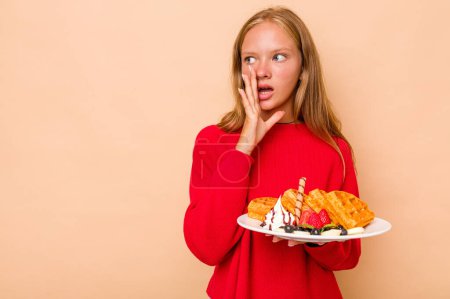 Photo for Little caucasian girl holding a waffles isolated on beige background is saying a secret hot braking news and looking aside - Royalty Free Image