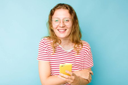 Téléchargez les photos : Jeune femme caucasienne tenant téléphone mobile isolé sur fond bleu rire et s'amuser. - en image libre de droit