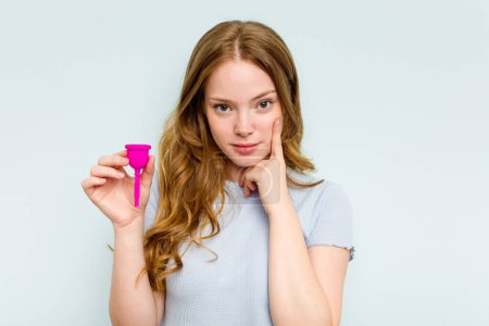 Téléchargez les photos : Jeune femme caucasienne tenant la coupe menstruelle isolée sur fond bleu pointant temple avec le doigt, pensant, concentré sur une tâche. - en image libre de droit