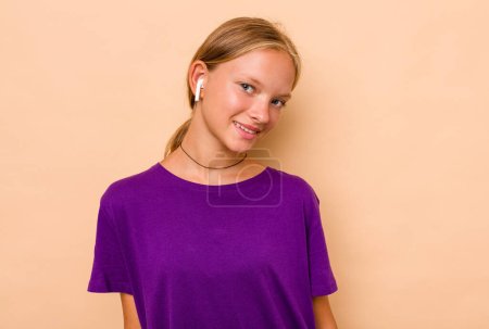 Téléchargez les photos : Petite fille caucasienne écoutant de la musique isolée sur fond beige - en image libre de droit