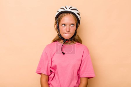 Photo for Little caucasian girl wearing a bike helmet isolated on beige background confused, feels doubtful and unsure. - Royalty Free Image