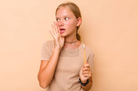 Foto de Caucásico adolescente chica cepillarse los dientes aislados en beige fondo gritando y sosteniendo la palma cerca de la boca abierta. - Imagen libre de derechos