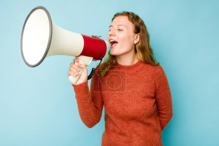 Foto de Mujer caucásica joven sosteniendo megáfono aislado sobre fondo azul gritando y sosteniendo la palma cerca de la boca abierta. - Imagen libre de derechos