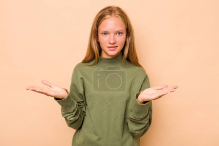 Téléchargez les photos : Caucasien adolescent fille isolé sur fond beige fait échelle avec les bras, se sent heureux et confiant. - en image libre de droit