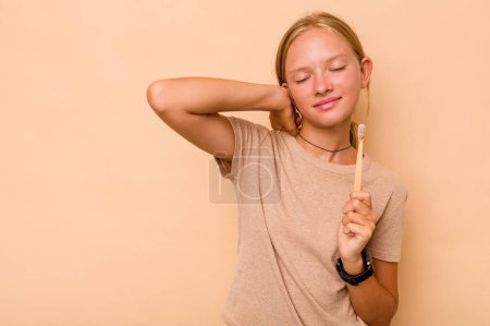 Foto de Caucásico adolescente chica cepillarse los dientes aislados en beige fondo tocando la parte posterior de la cabeza, pensando y haciendo una elección. - Imagen libre de derechos
