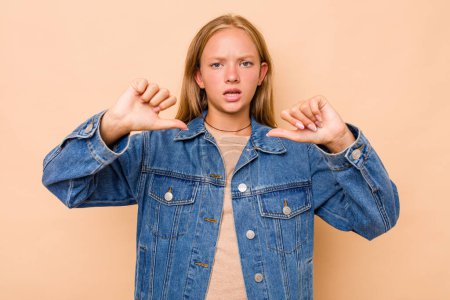 Foto de Caucásico adolescente chica aislado en beige fondo mostrando pulgar hacia abajo y expresando aversión. - Imagen libre de derechos