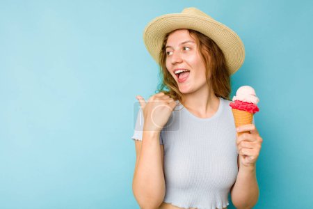 Photo for Young caucasian woman holding an ice cream isolated a blue background points with thumb finger away, laughing and carefree. - Royalty Free Image