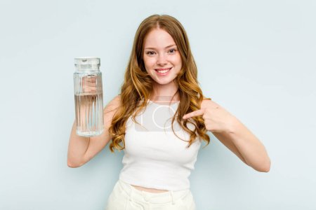 Foto de Joven mujer caucásica sosteniendo tarro de agua aislado sobre fondo azul persona señalando a mano a un espacio de copia de la camisa, orgulloso y seguro - Imagen libre de derechos
