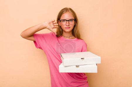 Téléchargez les photos : Petite caucasienne tenant une pizza isolée sur fond beige montrant un geste déplaisant, les pouces baissés. Concept de désaccord. - en image libre de droit