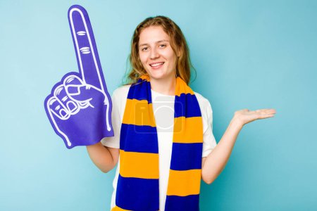 Téléchargez les photos : Jeune femme caucasienne fan de sport isolé sur fond bleu montrant un espace de copie sur une paume et tenant une autre main sur la taille. - en image libre de droit