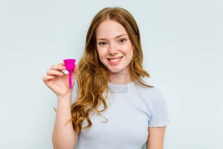 Téléchargez les photos : Jeune femme caucasienne tenant la coupe menstruelle isolée sur fond bleu heureux, souriant et joyeux. - en image libre de droit