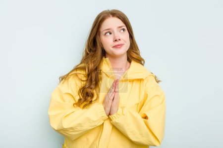 Téléchargez les photos : Jeune femme caucasienne isolée sur fond bleu tenant la main dans la prière près de la bouche, se sent confiante. - en image libre de droit