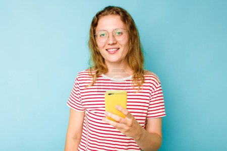 Foto de Joven mujer caucásica sosteniendo teléfono móvil aislado sobre fondo azul feliz, sonriente y alegre. - Imagen libre de derechos