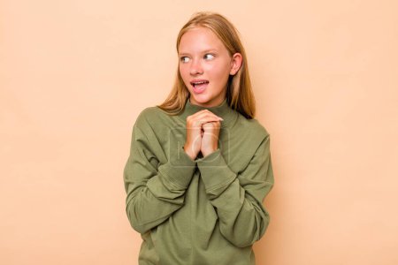 Photo for Caucasian teen girl isolated on beige background praying for luck, amazed and opening mouth looking to front. - Royalty Free Image