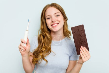 Téléchargez les photos : Jeune femme caucasienne tenant chocolat et brosse à dents isolés sur fond bleu - en image libre de droit