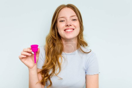 Foto de Joven mujer caucásica sosteniendo copa menstrual aislada sobre fondo azul riendo y divirtiéndose. - Imagen libre de derechos