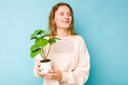 Photo for Young caucasian woman holding a plant isolated on blue background dreaming of achieving goals and purposes - Royalty Free Image