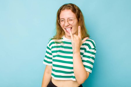 Photo for Young caucasian woman isolated on blue background showing rock gesture with fingers - Royalty Free Image