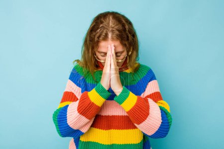 Foto de Joven mujer caucásica aislada sobre fondo azul rezando, mostrando devoción, persona religiosa buscando inspiración divina. - Imagen libre de derechos