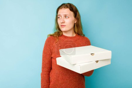 Photo for Young caucasian woman holding pizzas boxes isolated on blue background confused, feels doubtful and unsure. - Royalty Free Image