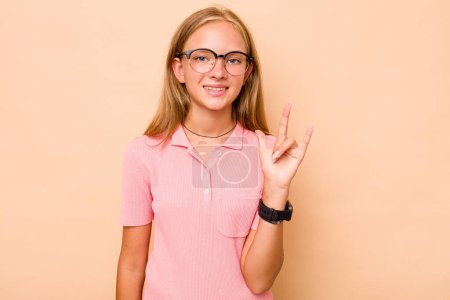 Foto de Caucásico adolescente chica aislada en beige fondo mostrando un gesto cuernos como un concepto de revolución. - Imagen libre de derechos