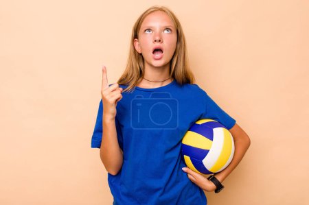 Foto de Niña caucásica jugando voleibol aislado sobre fondo beige apuntando al revés con la boca abierta. - Imagen libre de derechos