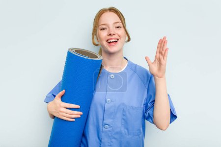 Photo for Young caucasian physiotherapist holding a mat isolated on blue background receiving a pleasant surprise, excited and raising hands. - Royalty Free Image