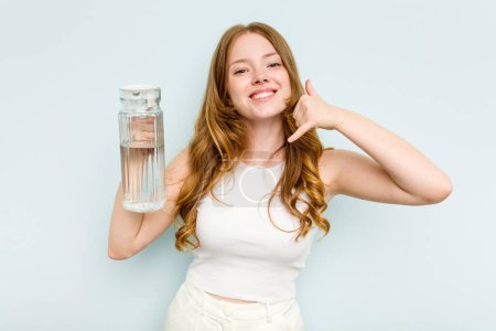 Téléchargez les photos : Jeune femme caucasienne tenant un pot d'eau isolé sur fond bleu montrant un geste d'appel téléphonique mobile avec les doigts. - en image libre de droit