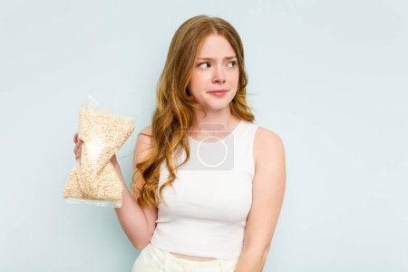 Photo for Young caucasian woman holding oatmeal isolated on blue background confused, feels doubtful and unsure. - Royalty Free Image