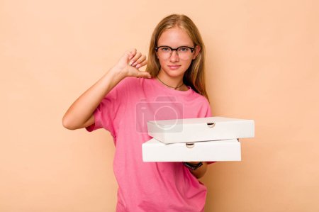 Téléchargez les photos : Petite fille caucasienne tenant pizza isolée sur fond beige se sent fière et confiante, exemple à suivre. - en image libre de droit