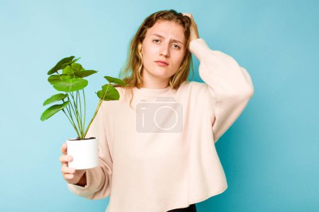 Photo for Young caucasian woman holding a plant isolated on blue background being shocked, she has remembered important meeting. - Royalty Free Image