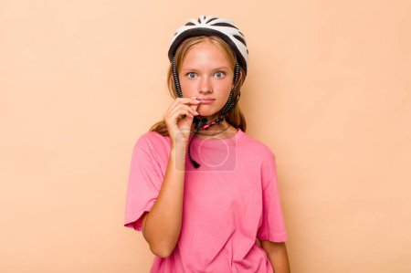 Foto de Pequeña chica caucásica con un casco de bicicleta aislado sobre fondo beige con los dedos en los labios manteniendo un secreto. - Imagen libre de derechos
