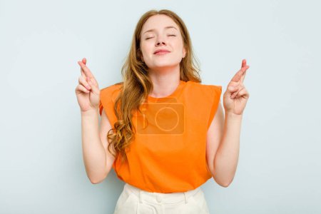 Téléchargez les photos : Jeune femme caucasienne isolée sur fond bleu croisant les doigts pour avoir de la chance - en image libre de droit