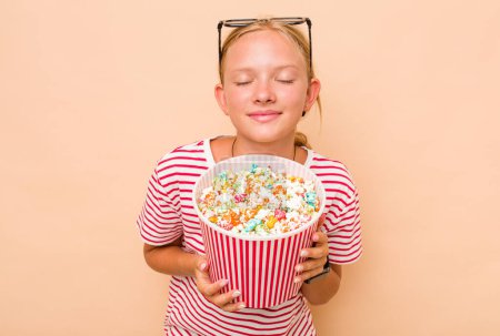 Téléchargez les photos : Petite fille caucasienne mangeant du pop-corn isolé sur fond beige - en image libre de droit