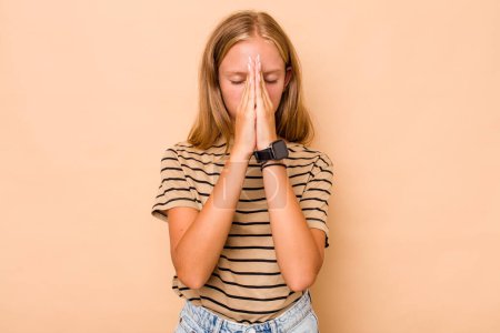 Photo for Caucasian teen girl isolated on beige background holding hands in pray near mouth, feels confident. - Royalty Free Image