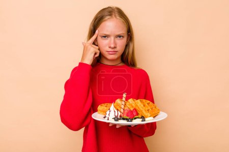 Photo for Little caucasian girl holding a waffles isolated on beige background showing a disappointment gesture with forefinger. - Royalty Free Image