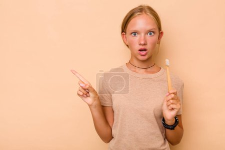 Foto de Caucásico adolescente chica cepillarse los dientes aislado en beige fondo apuntando a un lado - Imagen libre de derechos