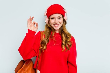 Photo for Young student woman wearing headphones isolated on blue background cheerful and confident showing ok gesture. - Royalty Free Image