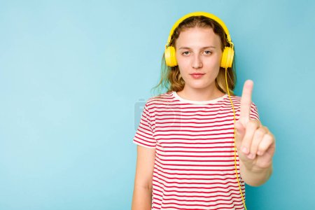 Téléchargez les photos : Jeune femme caucasienne portant des écouteurs isolés sur fond bleu montrant numéro un avec doigt. - en image libre de droit