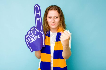 Téléchargez les photos : Jeune femme caucasienne fan de sport isolé sur fond bleu montrant poing à caméra, expression faciale agressive. - en image libre de droit