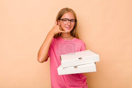 Foto de Pequeña chica caucásica sosteniendo pizza aislada sobre fondo beige mostrando un gesto de llamada de teléfono móvil con los dedos. - Imagen libre de derechos