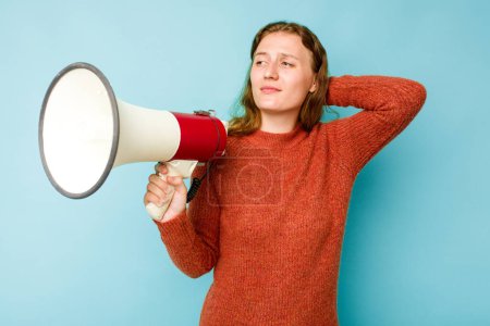 Téléchargez les photos : Jeune femme caucasienne tenant un mégaphone isolé sur fond bleu touchant l'arrière de la tête, pensant et faisant un choix. - en image libre de droit