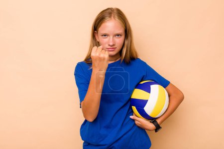 Téléchargez les photos : Petite fille caucasienne jouant au volley isolé sur fond beige montrant poing à caméra, expression faciale agressive. - en image libre de droit