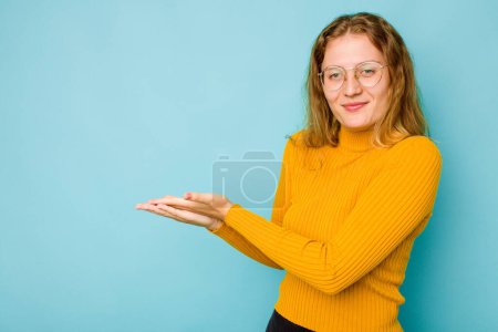 Foto de Mujer caucásica joven aislada sobre fondo azul sosteniendo un espacio de copia en una palma. - Imagen libre de derechos
